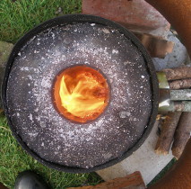 view of a home-made rocket stove from above, showing the insulation and the sticks feeding the flames