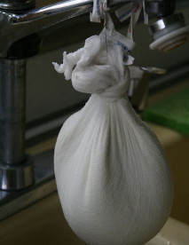 Draining the whey from the cheese by hanging it in a cheesecloth over a sink